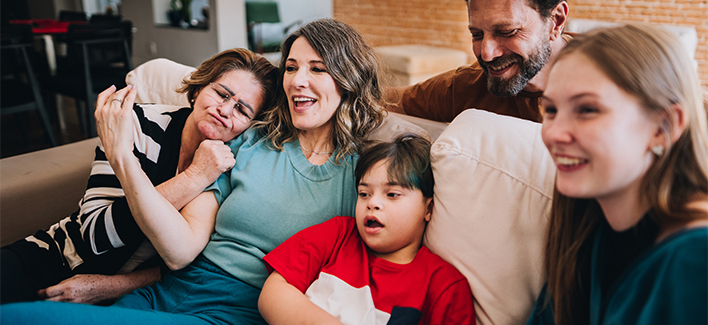 A happy family, including a child with down syndrome, enjoying quality time together, watching TV on the couch.